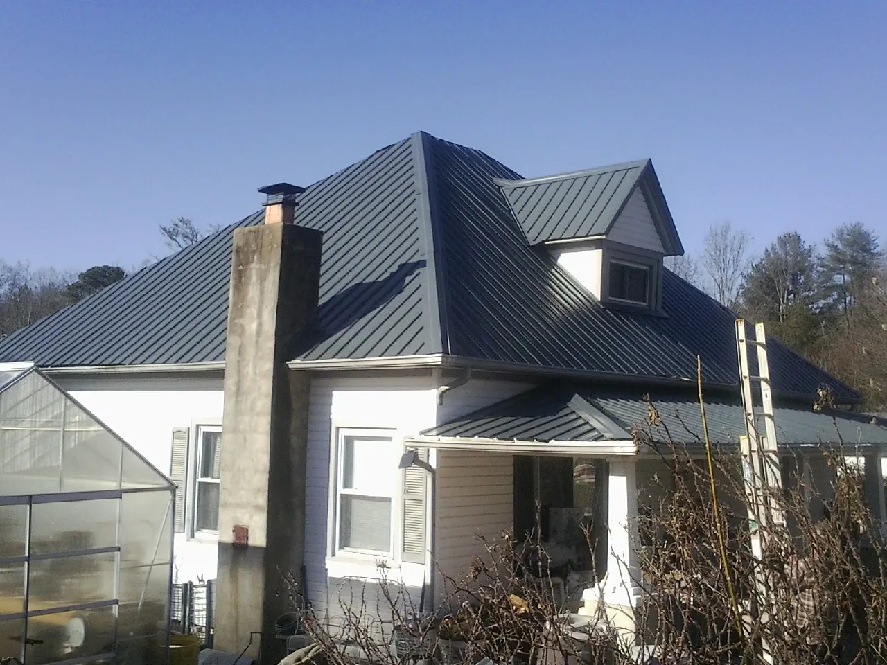 Dark blue standing seam metal roof on a white farmhouse with dormer — Slate & Tile Roof Repair by Roofing Brothers in Kannapolis