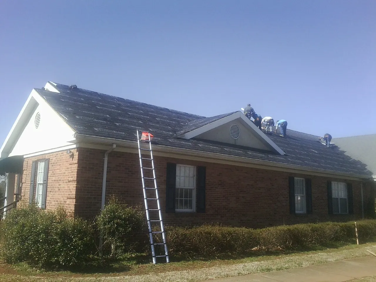 Crew tearing shingles off a brick ranch roof with a ladder set — Emergency Roof Repair work by our crew in Kannapolis