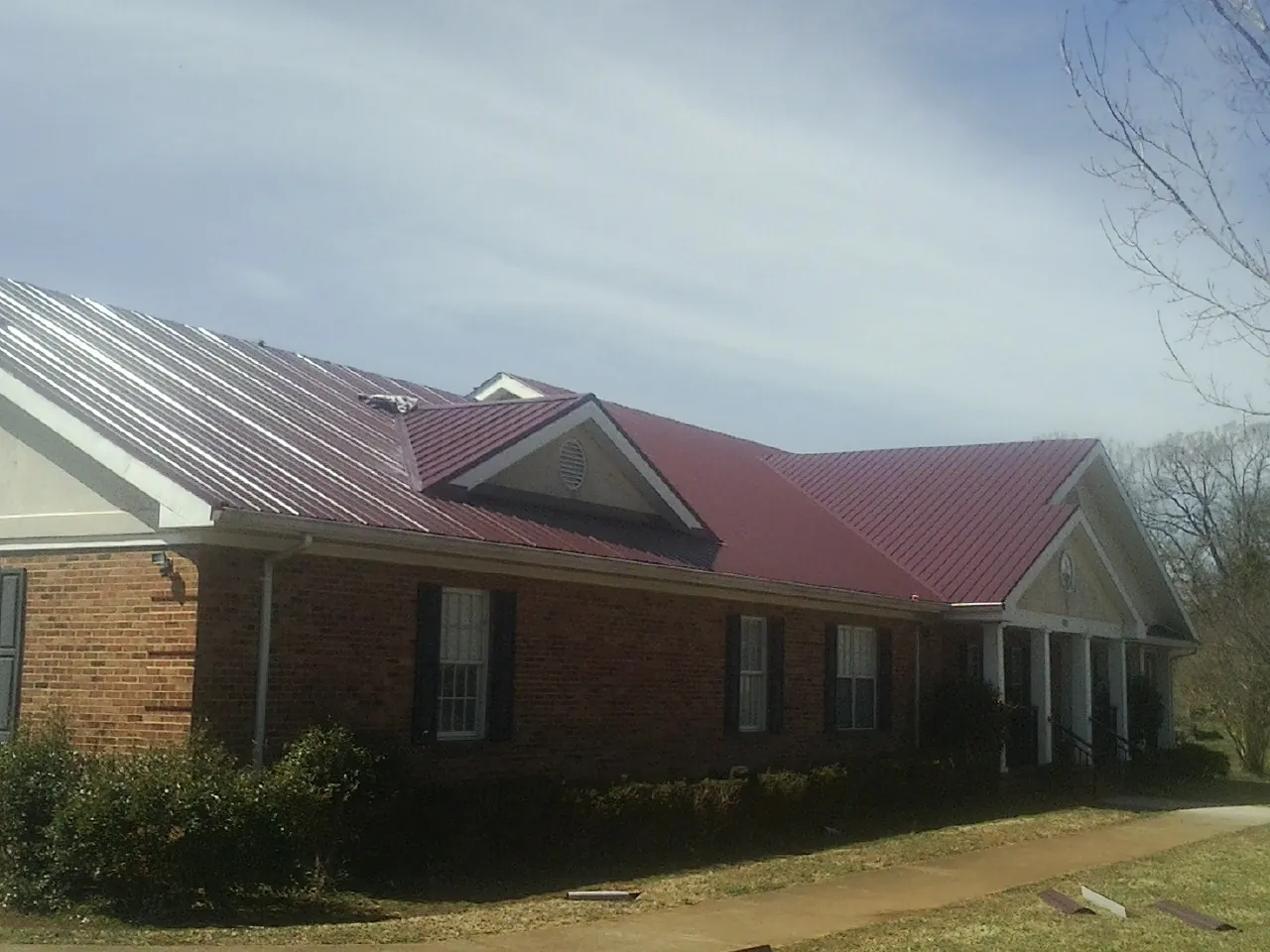 Red metal roof with gabled entries on a long brick building, from a Hail Damage Roof Repair job in Kannapolis