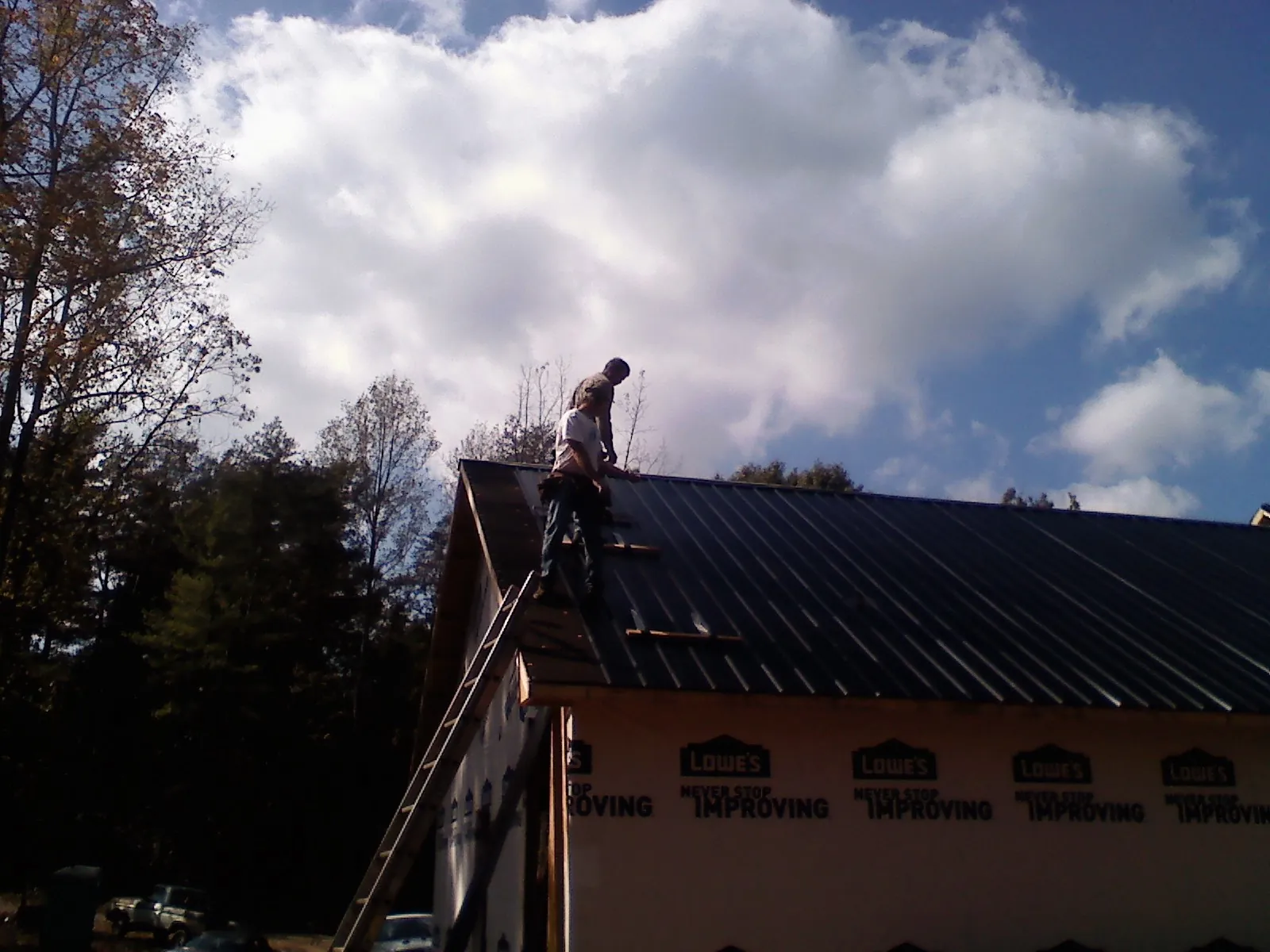 Roofer fastening dark metal panels high against a cloudy sky, from a Roof Inspection job in Kannapolis