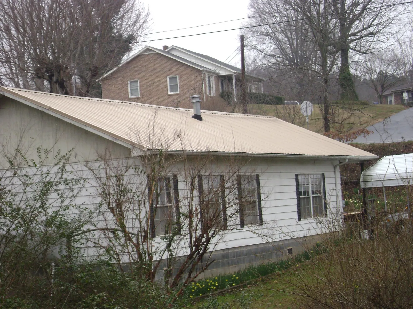 Tan metal roof on a white sided house set into a hillside — Commercial Roofing by Roofing Brothers in Kannapolis