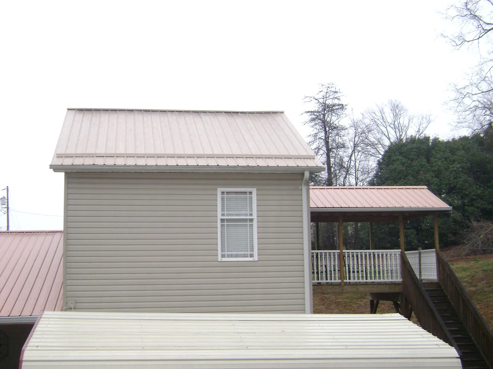 Tan metal roofs on a two story addition and attached porch, from a Roof Replacement job in Kannapolis